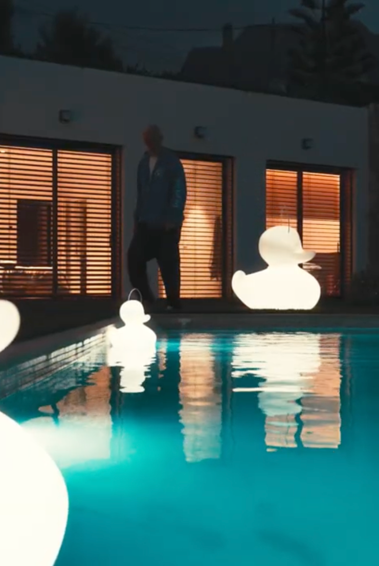 Goodnight Light Duck-Duck lamps glowing in infinity pool at night, Mediterranean home setting