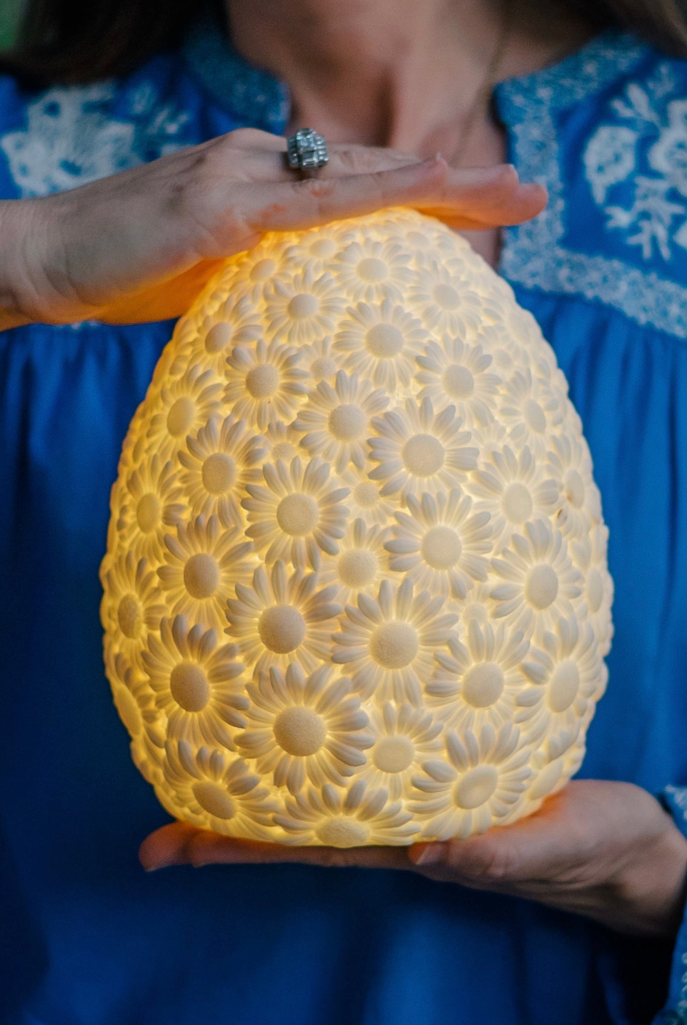 Goodnight Light Daisy lamp glowing between a pair of hands, offering a gift