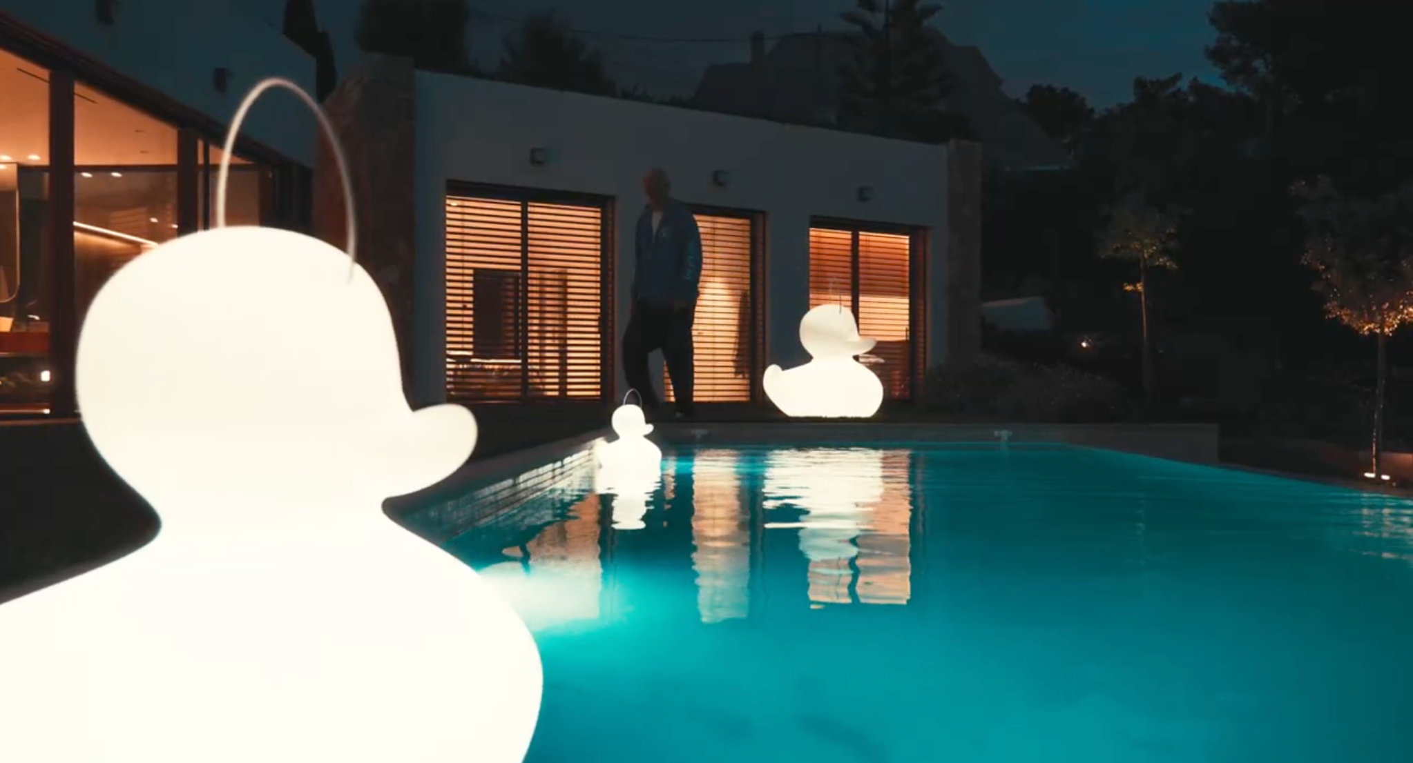 Goodnight Light Duck-Duck lamps glowing in infinity pool at night, Mediterranean home setting