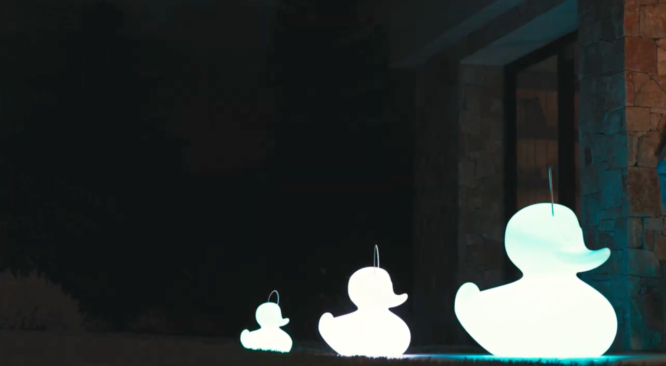 Goodnight Light Duck Duck lamp in three sizes on the terrace in front of a villa, lights on glowing 
