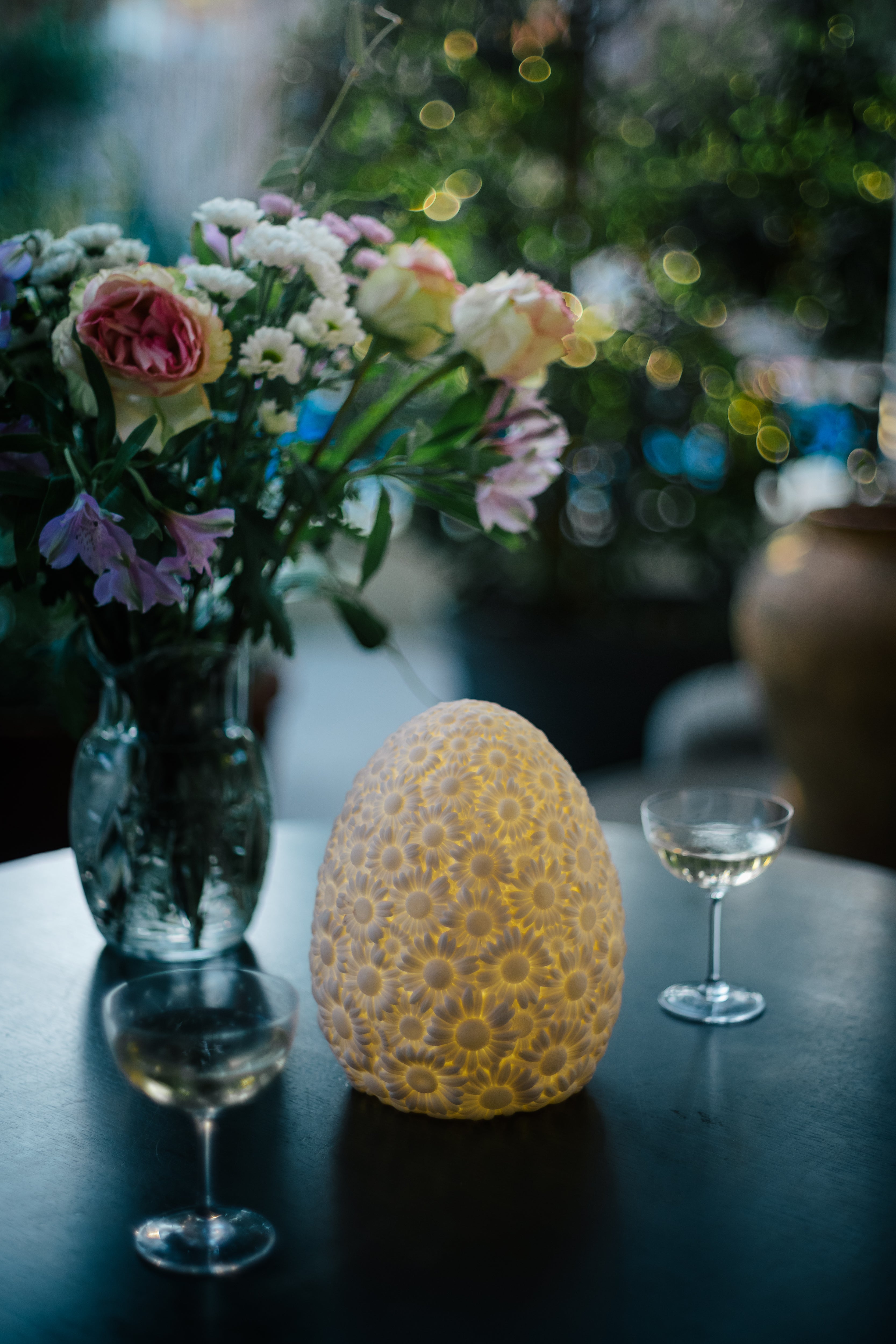 Goodnight Light Daisy lamp on a table with two wine glasses and a bouquet of flowers, glowing